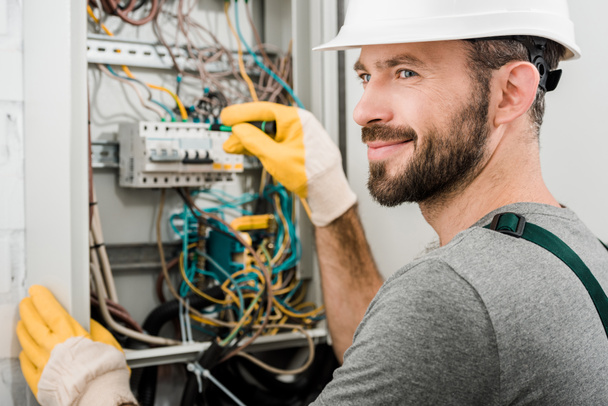 stock photo handsome cheerful electrician repairing electrical box using screwdriver corridor